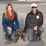 A man and woman kneeling on the ground with a dog in the middle smiling for a picture