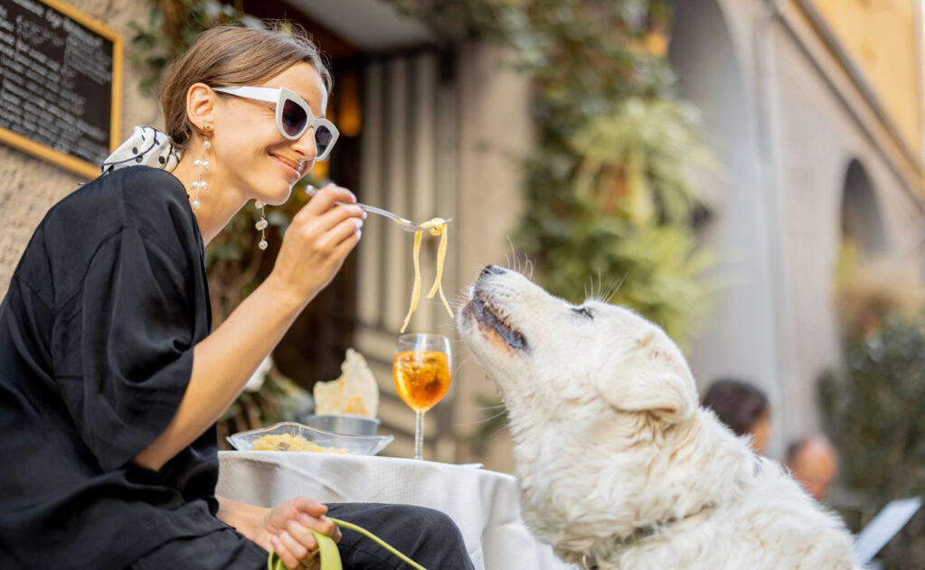 A woman feeding dog pasta at a restaurant