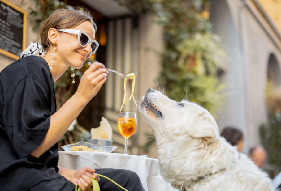 A woman feeding dog pasta at a restaurant