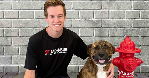 A young man smiles next to a happy dog, with a red fire hydrant in the background.