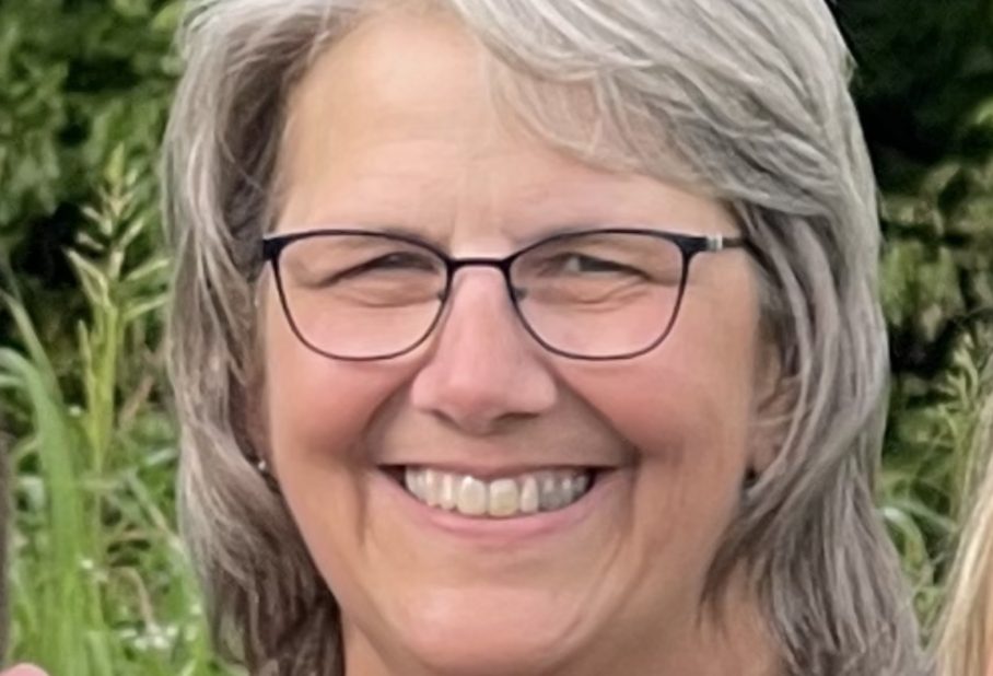 A woman with grey hair wearing glasses smiling for a picture