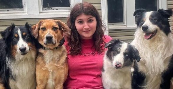 A girl and 4 dogs sitting smiling for a photo