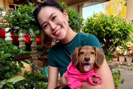 A woman holding a puppy smiling for a photo