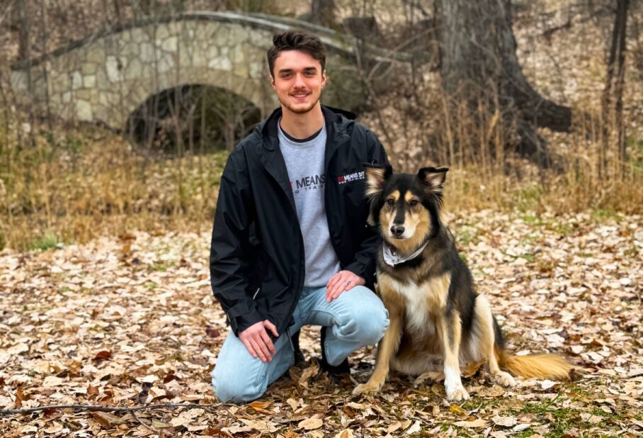 Keeyan, a professional dog trainer from Sit Means Sit Pueblo, standing on a grassy field outdoors, smiling confidently while holding a red leash, showcasing his approachable demeanor and expertise in dog training services.