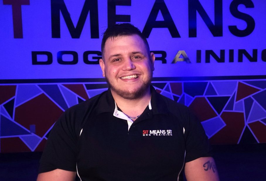 a man smiling for a photo with a sit means sit sign on the background