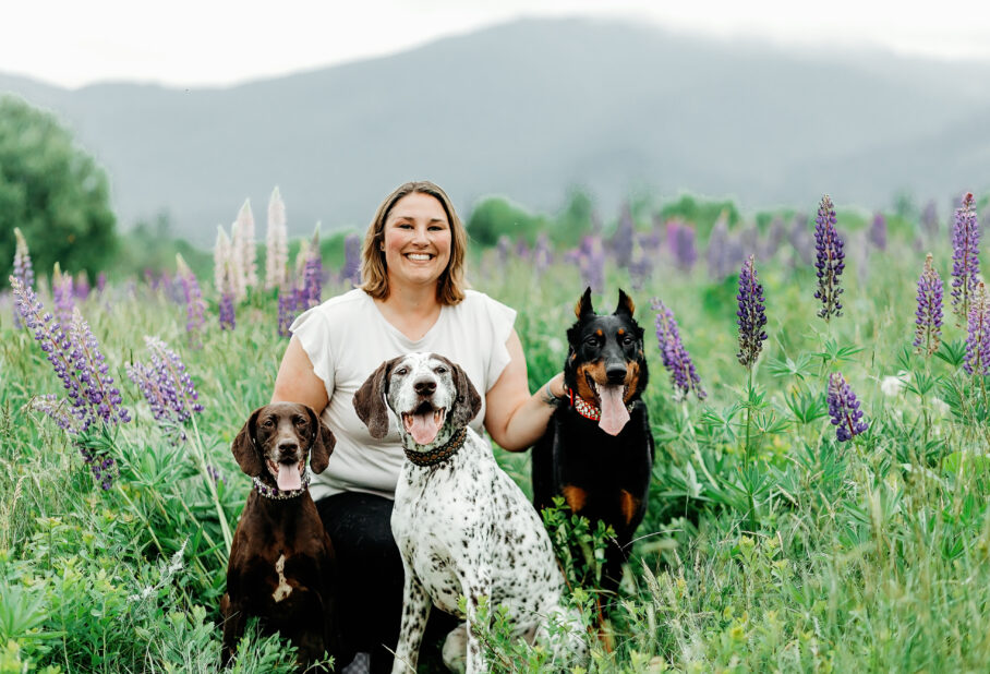 A woman and three dogs sitting in a field smiling for a photo